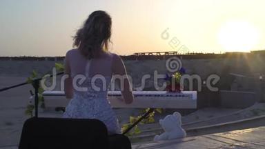 年轻的金发女人在日落时用数字钢琴演奏浪漫的音乐。 漂亮女孩在舞台上和太阳一起唱歌